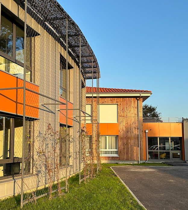 Bâtiment moderne avec treillis et plantes grimpantes, façades en bois et orange, sous ciel bleu à Rochefort en Charente-Maritime 17