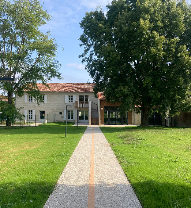 Chemin en gravier menant à un bâtiment en pierre avec des volets blancs, entouré d'herbe et d'arbres à Rochefort en Charente-Maritime 17