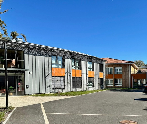 Deux bâtiments modernes, un gris et orange, l'autre en bois, sous un ciel bleu clair à Rochefort en Charente-Maritime 17