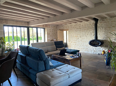 Salon rustique avec murs en pierre, canapé modulable, et poêle à bois suspendu à Rochefort en Charente-Maritime 17