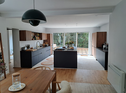 Cuisine moderne ouverte avec îlot central, placards en bois et noirs, vue sur jardin à Rochefort en Charente-Maritime 17